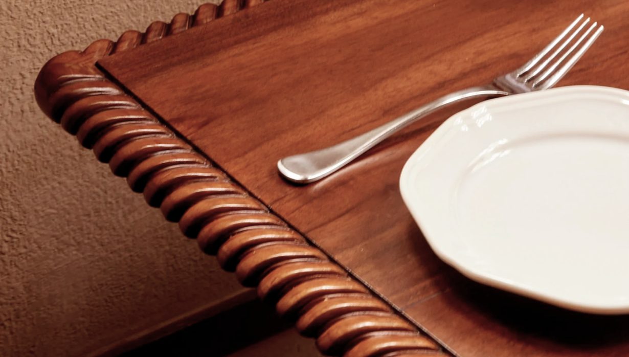 A carved wooden table set with a fork and white plate